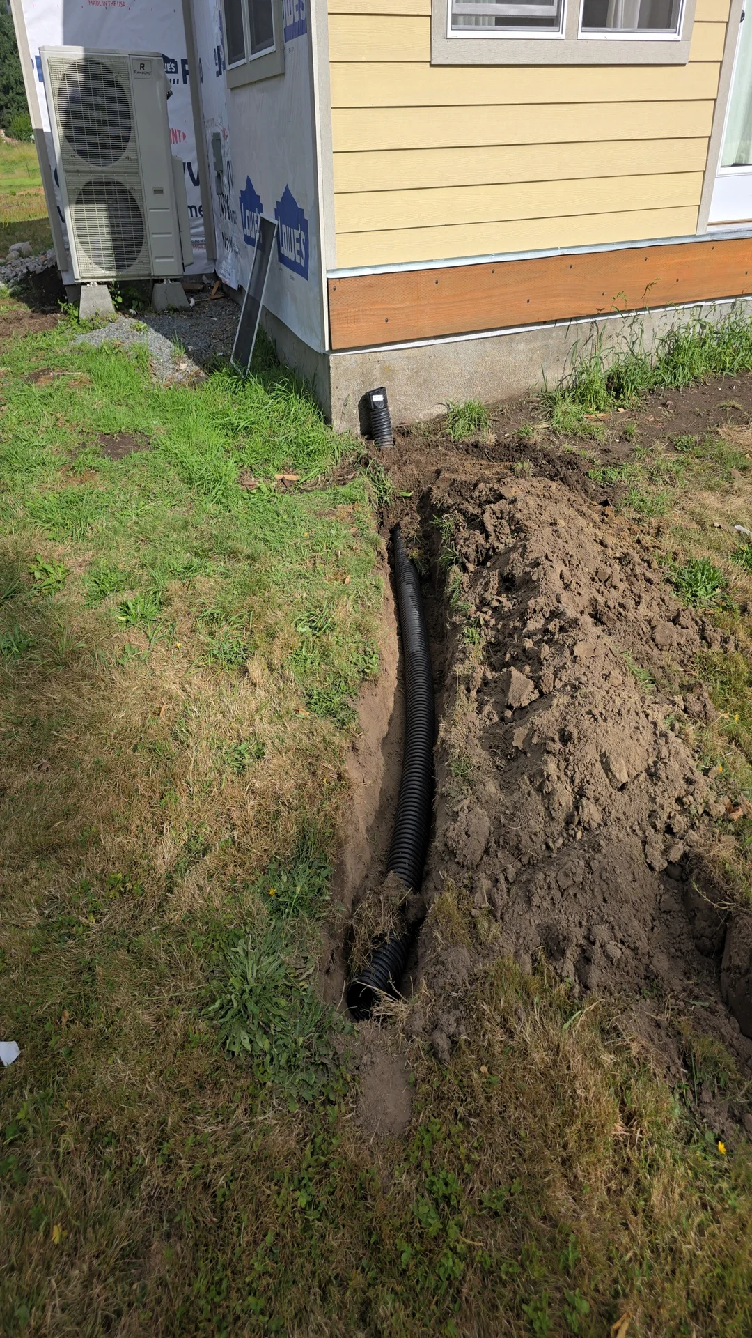 Black perforated drainage pipe installed in trench along residential foundation