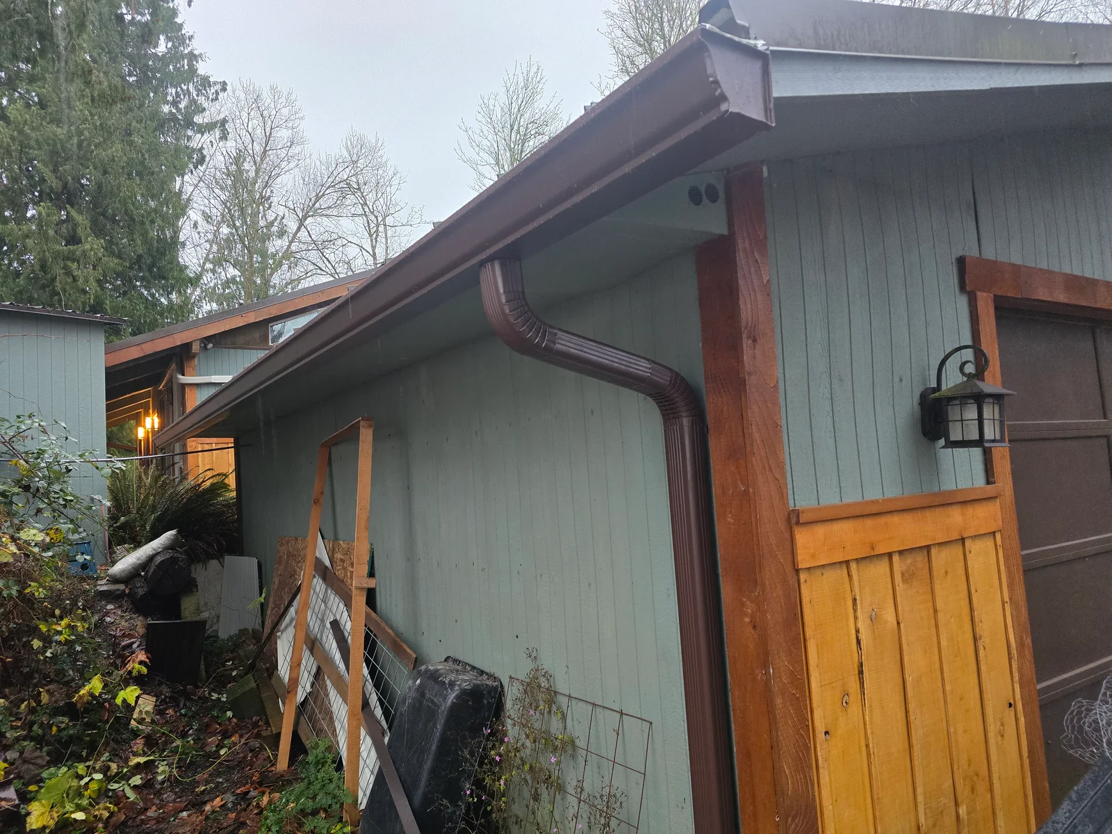 Brown seamless gutter with downspout and fascia trim on residential roofline