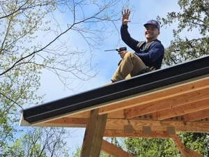 Two technicians installing black seamless gutters and downspout on wood pergola structure