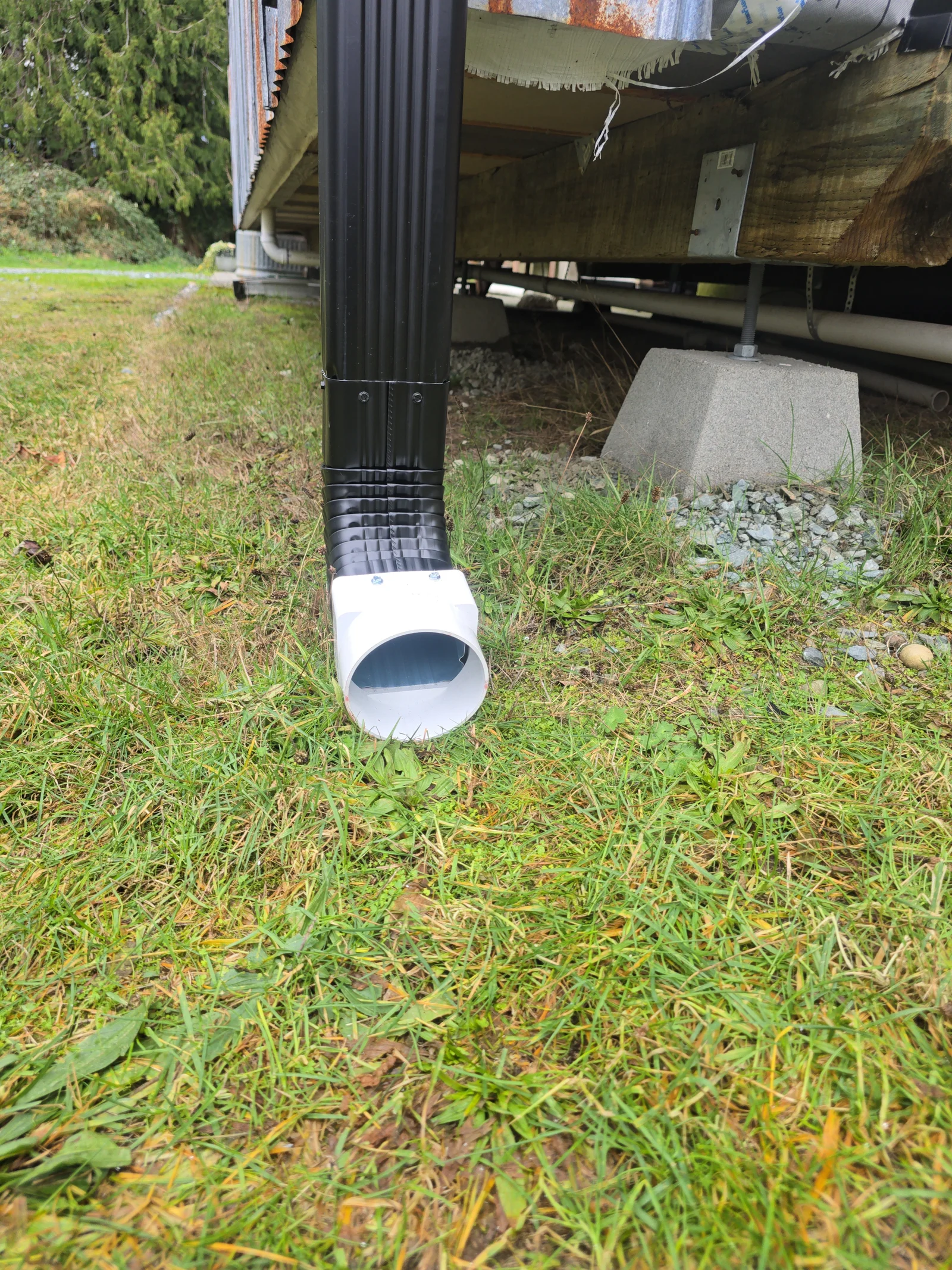 Black corrugated downspout with white elbow and concrete splash block on gravel base