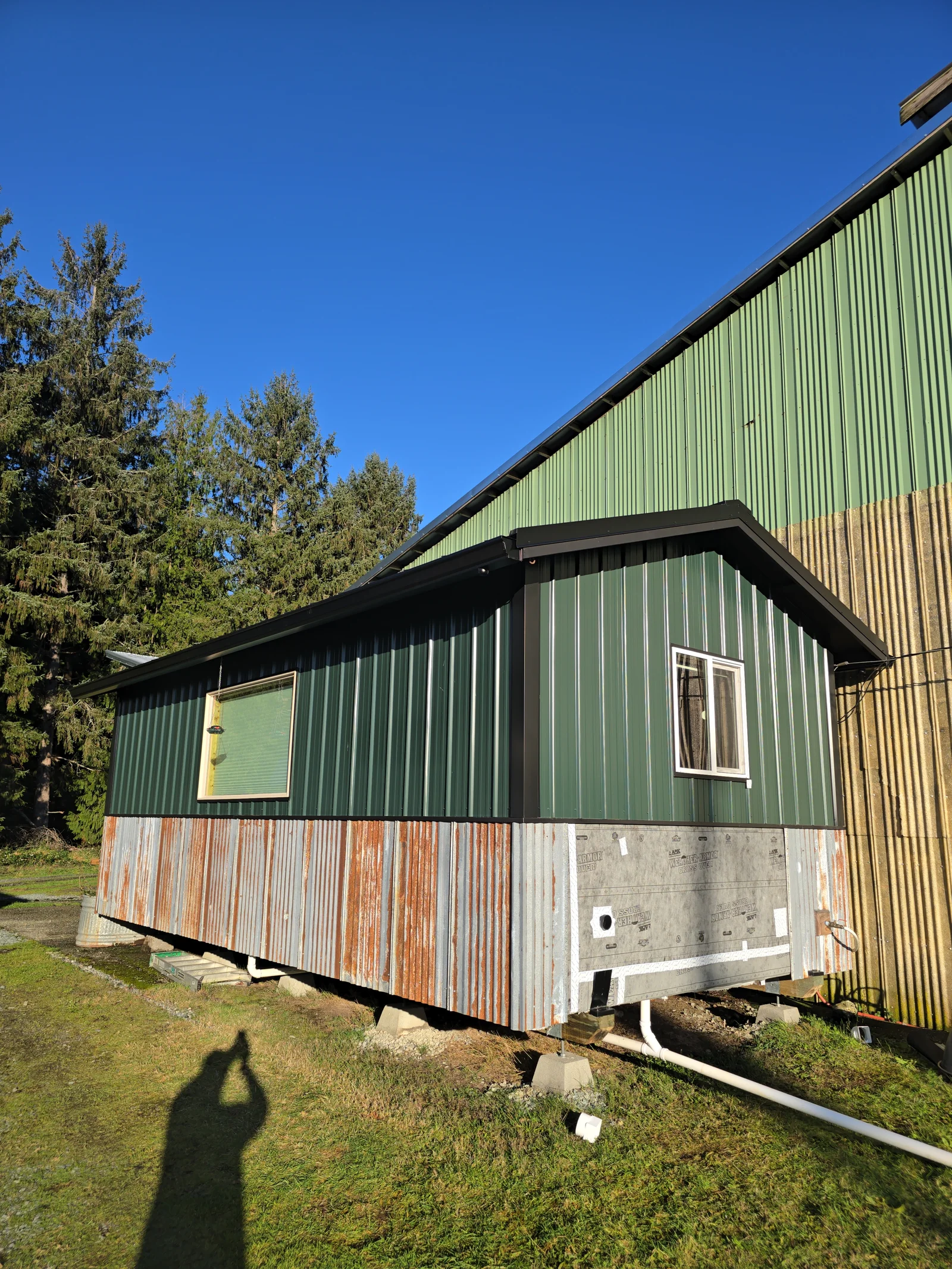 Metal corrugated siding with white gutters and downspout drainage system on residential foundation