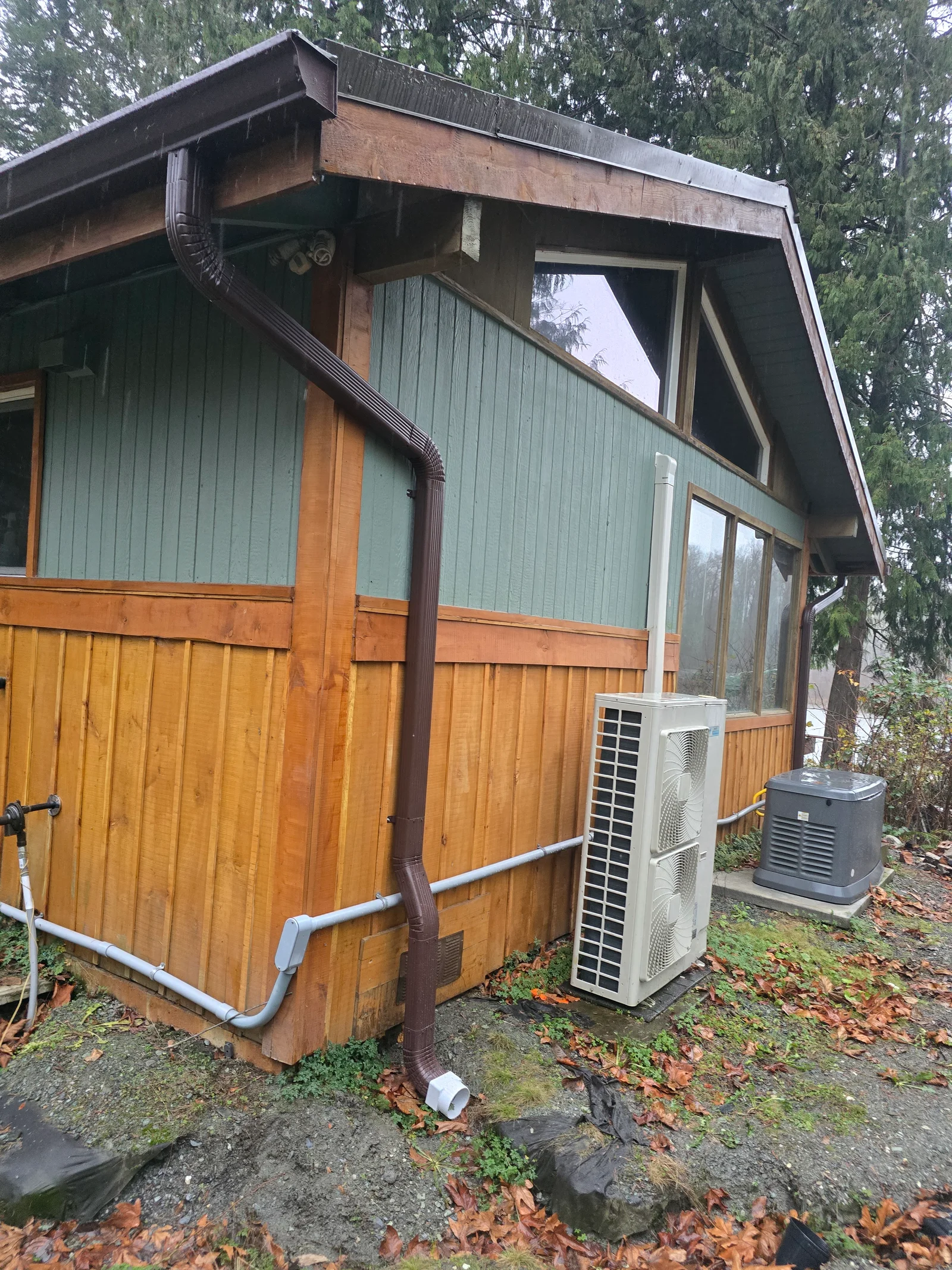 Dark metal gutters and downspout on wood-sided residential building with proper drainage routing