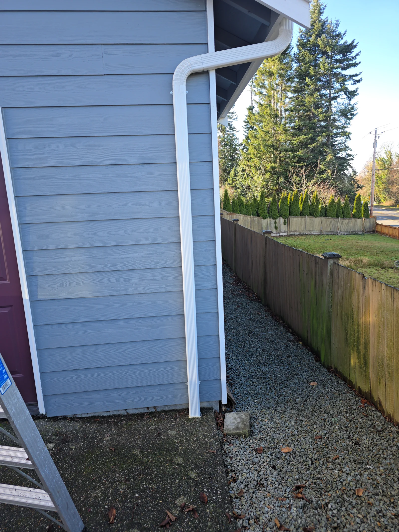 White seamless aluminum gutter with curved downspout extension on blue siding
