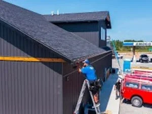 Gutter installation on residential roof with dark guttering system and professional ladder setup
