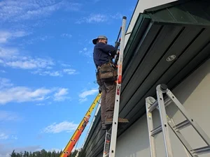 Worker installing seamless gutters from elevated lift platform on residential roofline