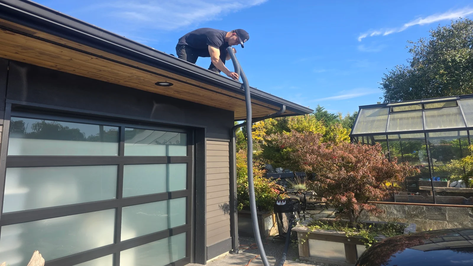 Technician cleaning gutters on residential home with metal-framed garage door and wood soffit